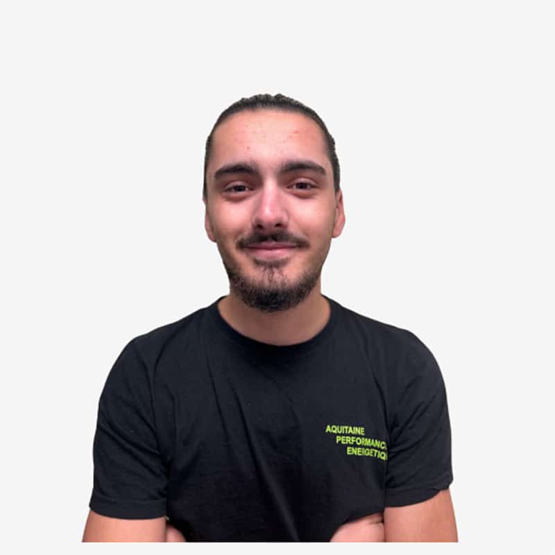 Portrait Employé T-shirt Aquitaine Performance Énergétique Jeune homme souriant avec une petite barbe et les cheveux tirés, portant un t-shirt noir avec l'inscription jaune fluo « AQUITAINE PERFORMANCE ENERGETIQ ».